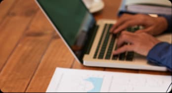 Hands typing on a laptop at a wooden desk beside a printed financial chart